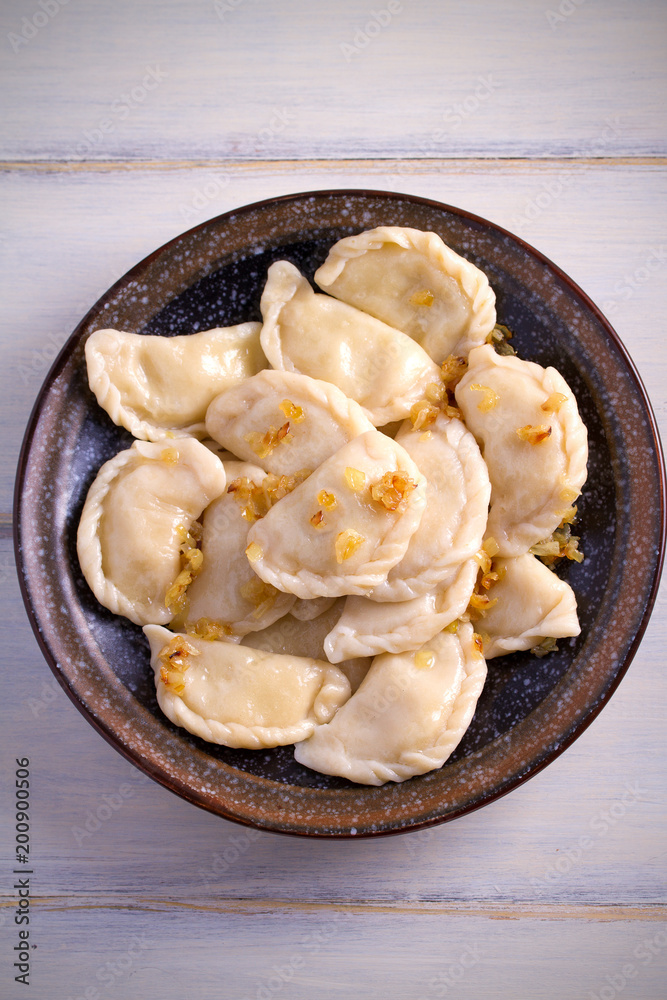 Pierogi or pyrohy, varenyky, vareniki, dumplings served with caramelized salted onion in bowl on wooden table. vertical Pierogi or pyrohy, varenyky, vareniki, dumplings served with caramelized salted onion in bowl on wooden table. vertical