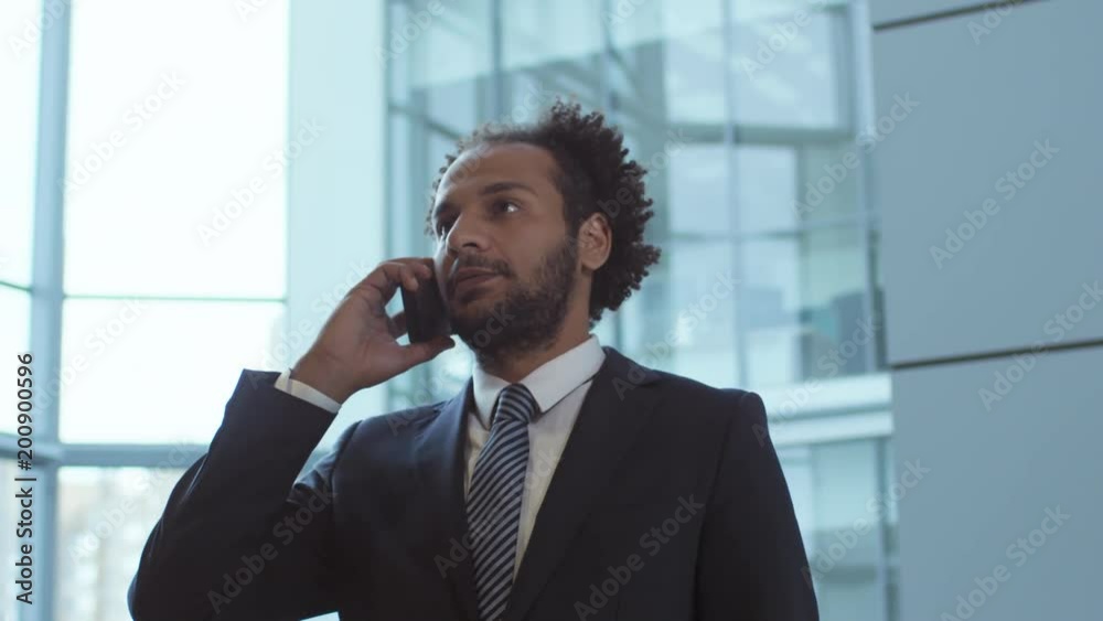 Tilt up shot of middle eastern entrepreneur standing in business center and answering phone call