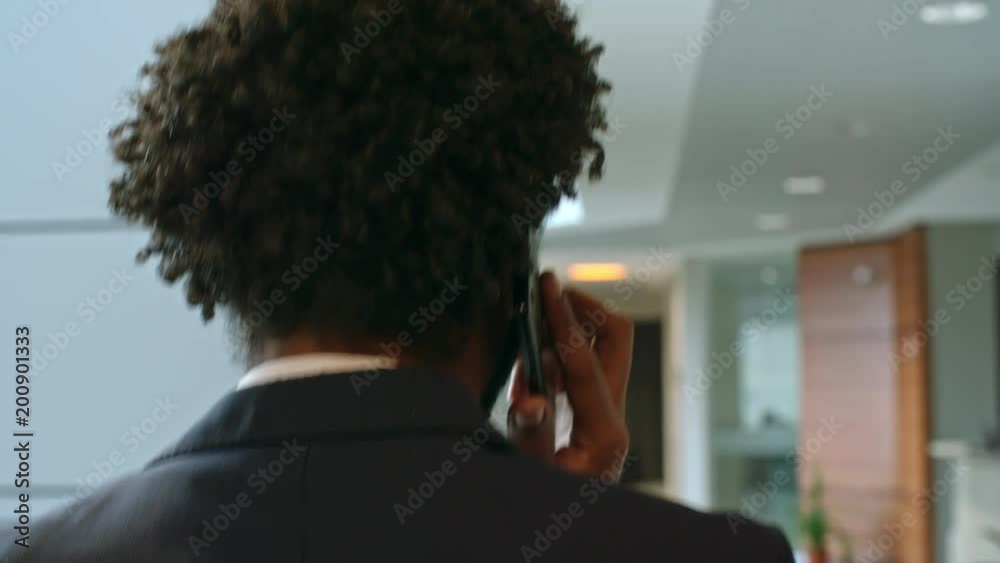 Rear view of businessman walking through office center and talking on cell phone Rear view of businessman walking through office center and talking on cell phone