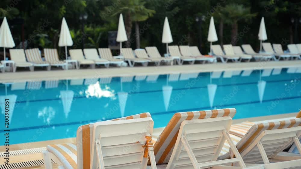 Sun loungers beside pool without people in yard of hotel in early morning. Tropical summer landscape Sun loungers beside pool without people in yard of hotel in early morning. Tropical summer landscape