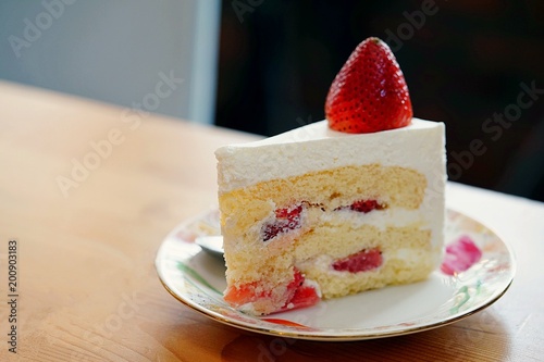 A strawberry shortcake topped with a large fresh strawberry placed in white plate and on wooden table with copy space.Victorian sponge cake with cream and strawberries.