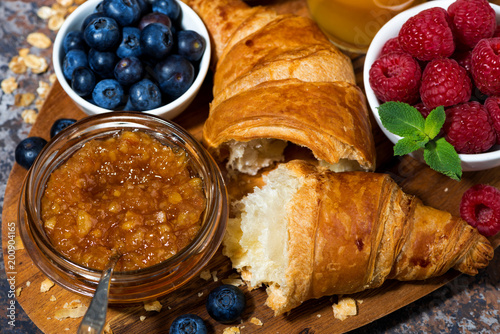 croissant, orange jam and fresh berries on a wooden board