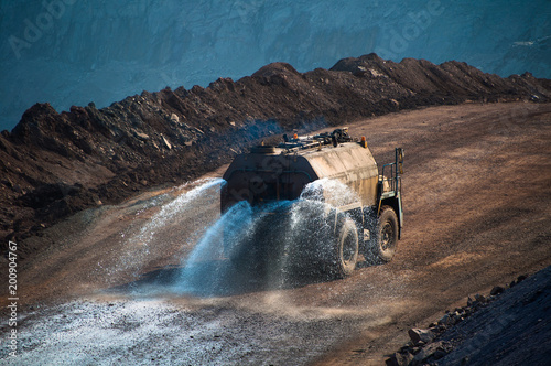 Heavy truck pours the road with water in the iron ore quarry. Dust removal, protection of the environment. Irrigation of the road from dust