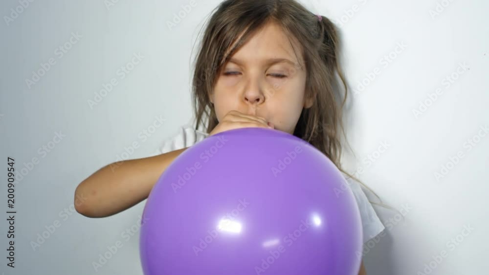 Medium shot of little girl looking at camera and trying to blow up purple balloon for party decoration Medium shot of little girl looking at camera and trying to blow up purple balloon for party decoration