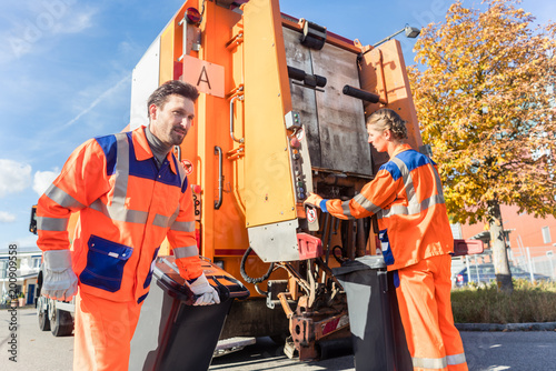 Waste collector gripping handle of garbage truck riding on the platform