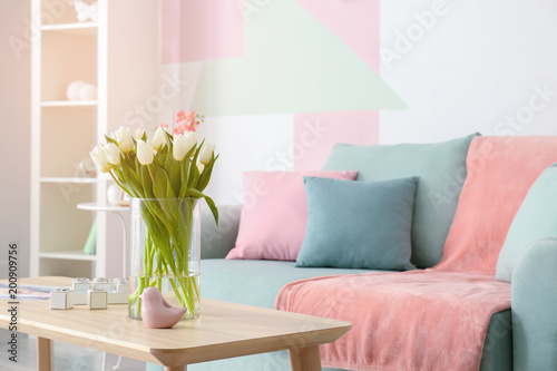 Wooden table with bouquet of tulips near sofa in living room