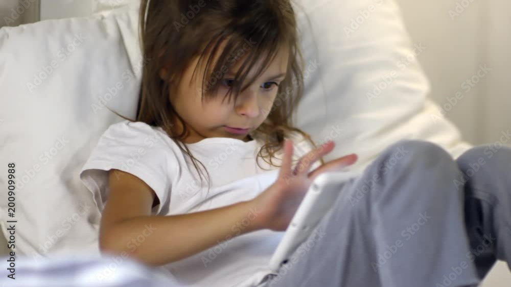 Medium shot of girl of primary school age sitting on bed and leaning on pillow when using laptop computer Medium shot of girl of primary school age sitting on bed and leaning on pillow when using laptop computer