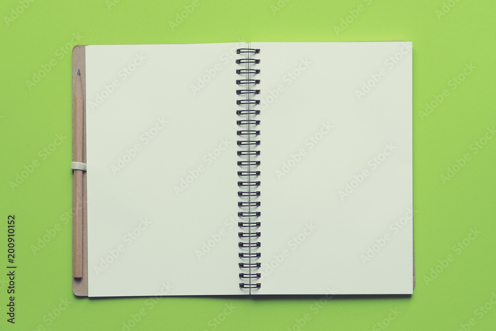 Notebook with a wooden pencil on green background, close up Notebook with a wooden pencil on green background, close up