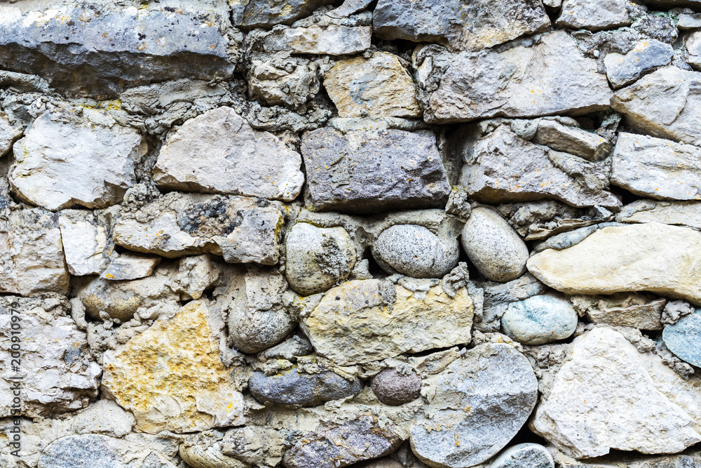 Background of grey and brown stonework wall with different forms stones and rough texture