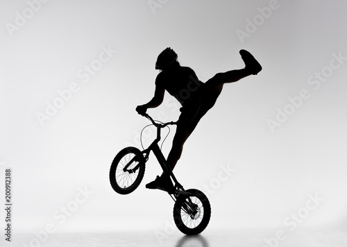silhouette of trial biker performing stunt on bicycle on white