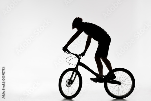silhouette of trial biker in helmet balancing on bicycle on white