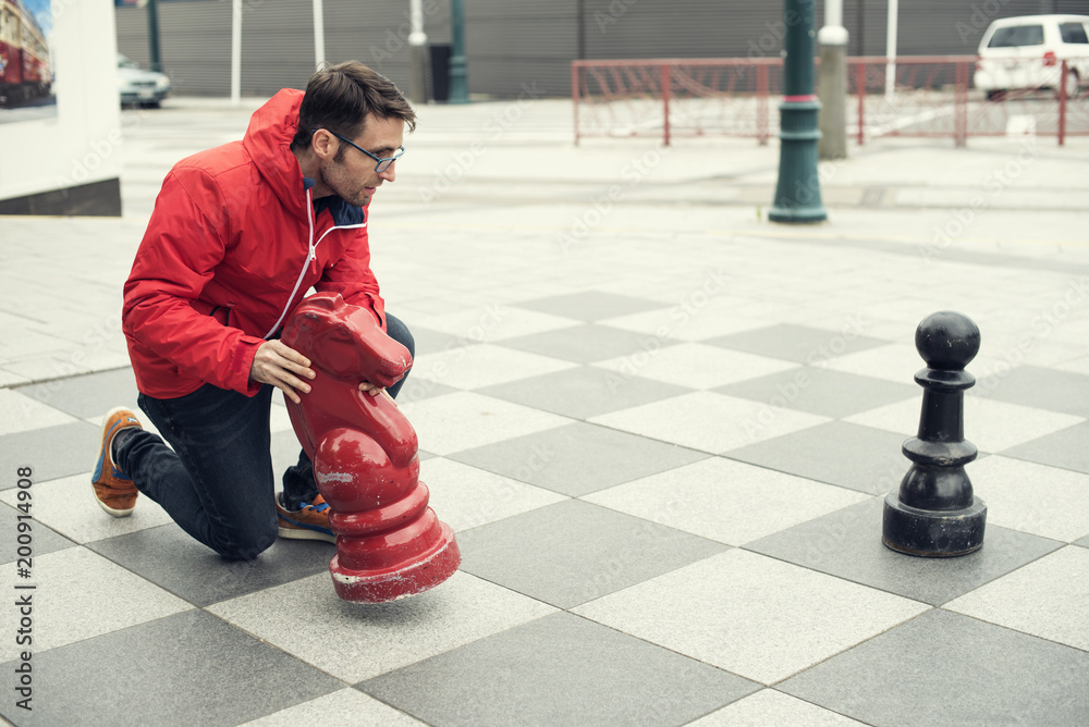 Hombre joven con chaquetón rojo jugando al ajedrez con piezas gigantes  Stock Photo | Adobe Stock