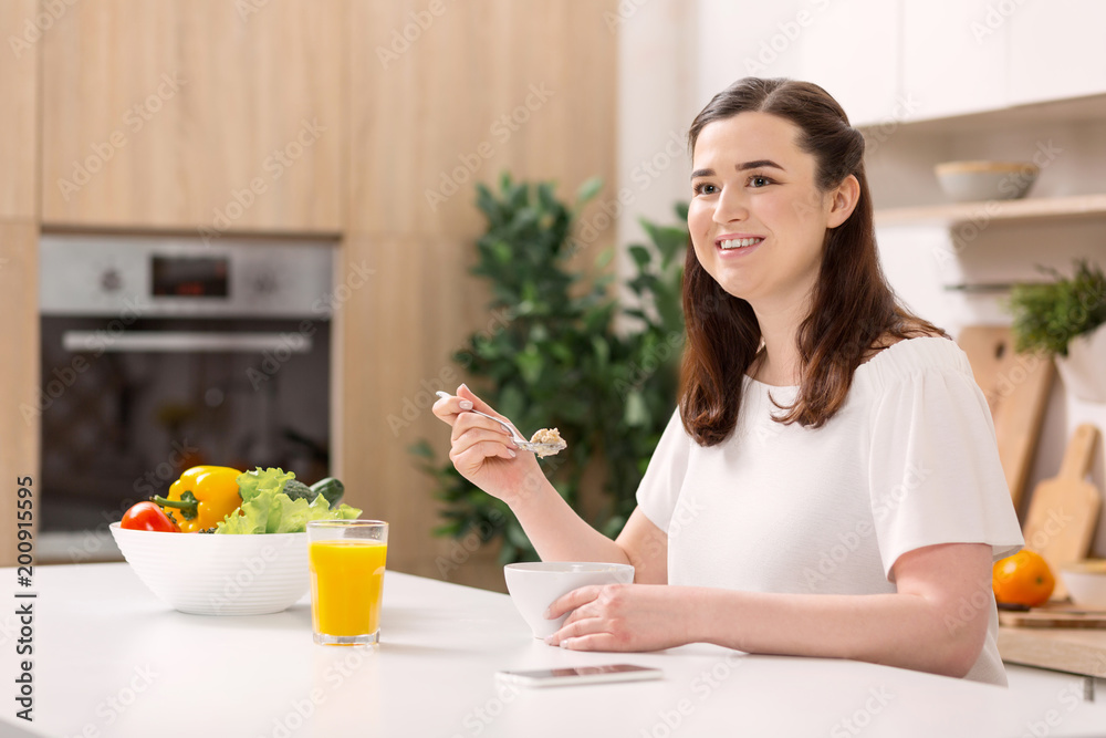 Nutritious breakfast. Satisfied pretty woman consuming porridge while grinning