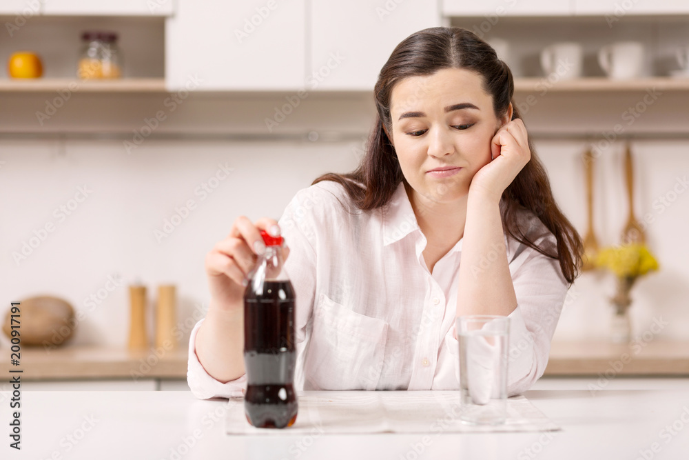 Favorite beverage. Upset melancholy woman touching bottle while staring down Favorite beverage. Upset melancholy woman touching bottle while staring down