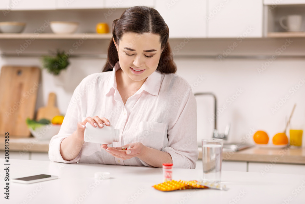 Support your body. Pleased gay woman looking down while taking medications Support your body. Pleased gay woman looking down while taking medications
