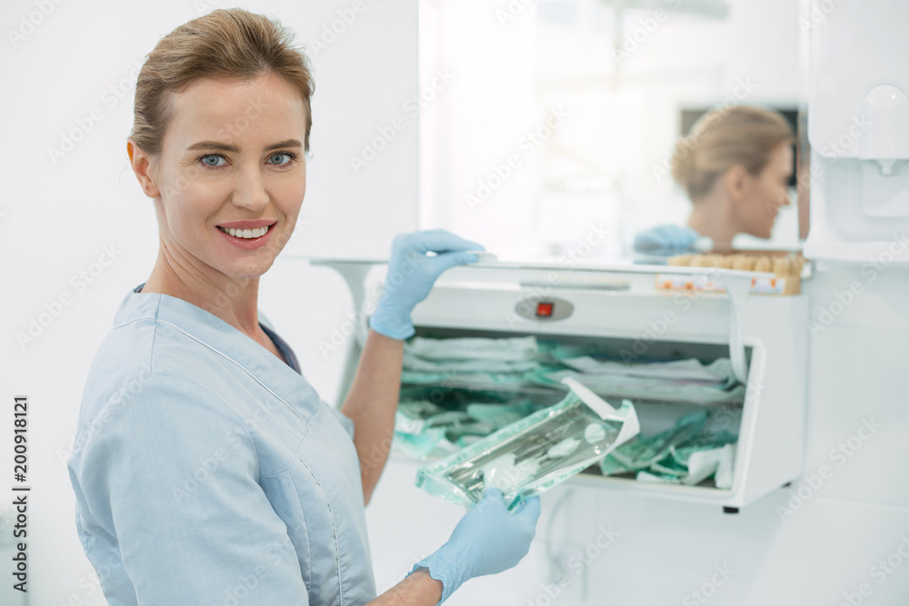 Fototapeta premium In high spirits. Inspired professional dentist smiling and holding some instruments