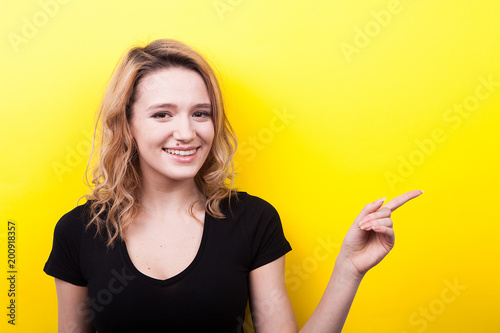 Happy beautiful young woman pointing on the side on yellow background in studio photo