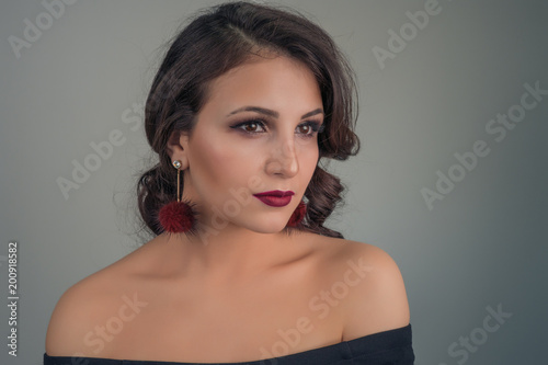 Portrait of a young beautiful sexy brunette with bright earrings on a gray background