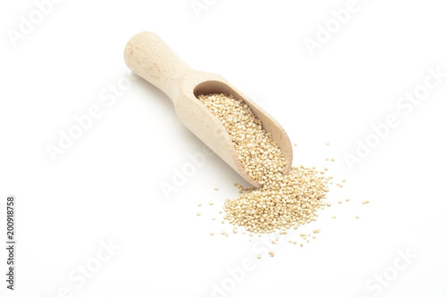 Semillas de quinoa cruda en una cuchara de madera sobre fondo blanco