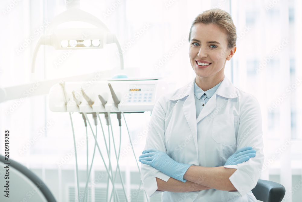 © Viacheslav Yakobchuk - Feeling inspired. Joyful female dentist smiling and standing with her arms crossed