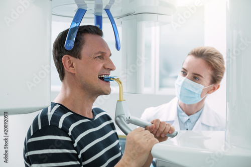 Improving teeth. Serious dark-haired man opening his mouth and having a dental device in it