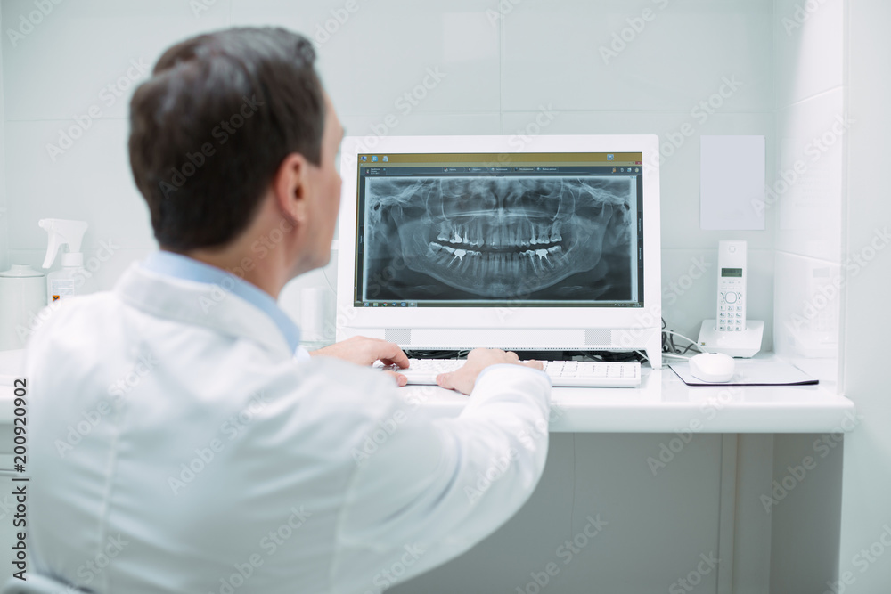 My powerful device. Determined male dentist wearing a uniform and working on his new device My powerful device. Determined male dentist wearing a uniform and working on his new device