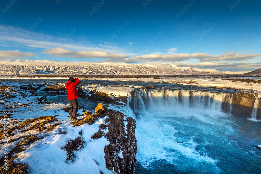 Photoghaper taking a photo at Godafoss waterfall in winter, Iceland. - obrazy, fototapety, plakaty 