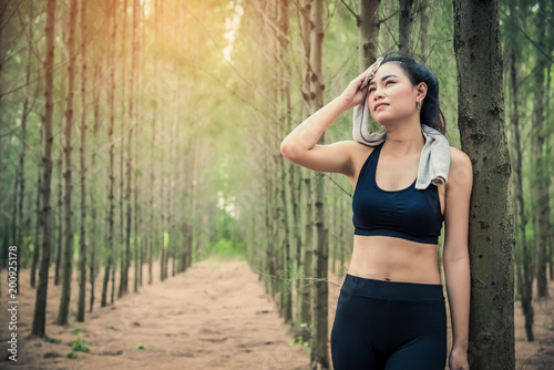 Asian beauty woman wiping the sweat in forest. Towel and sweat elements. Sport and Healthy concept. Jogging and Running concept. Relax and take a break theme. Outdoors activity theme.