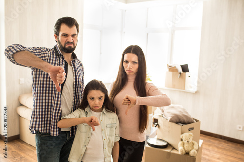 Sad and unsatisfied family are standing in the room. They don't like the house they bought. People are showing their thumbs down.