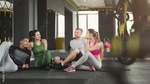 Group of sporty people sitting on floor at gym