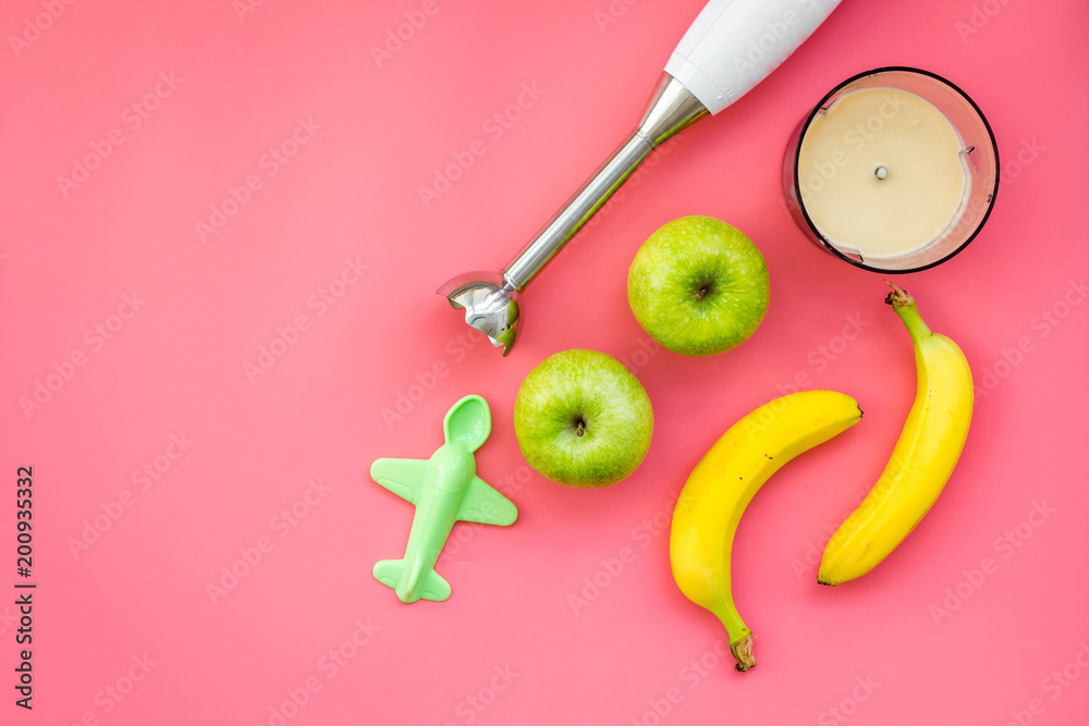 Homemade baby food. Cook puree with apple and banana with immersion blender. Pink background with toy top view space for text Homemade baby food. Cook puree with apple and banana with immersion blender. Pink background with toy top view space for text