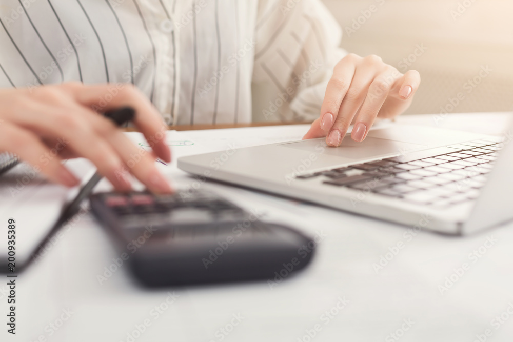 Closeup of woman hands counting on calculator and typing on laptop Closeup of woman hands counting on calculator and typing on laptop