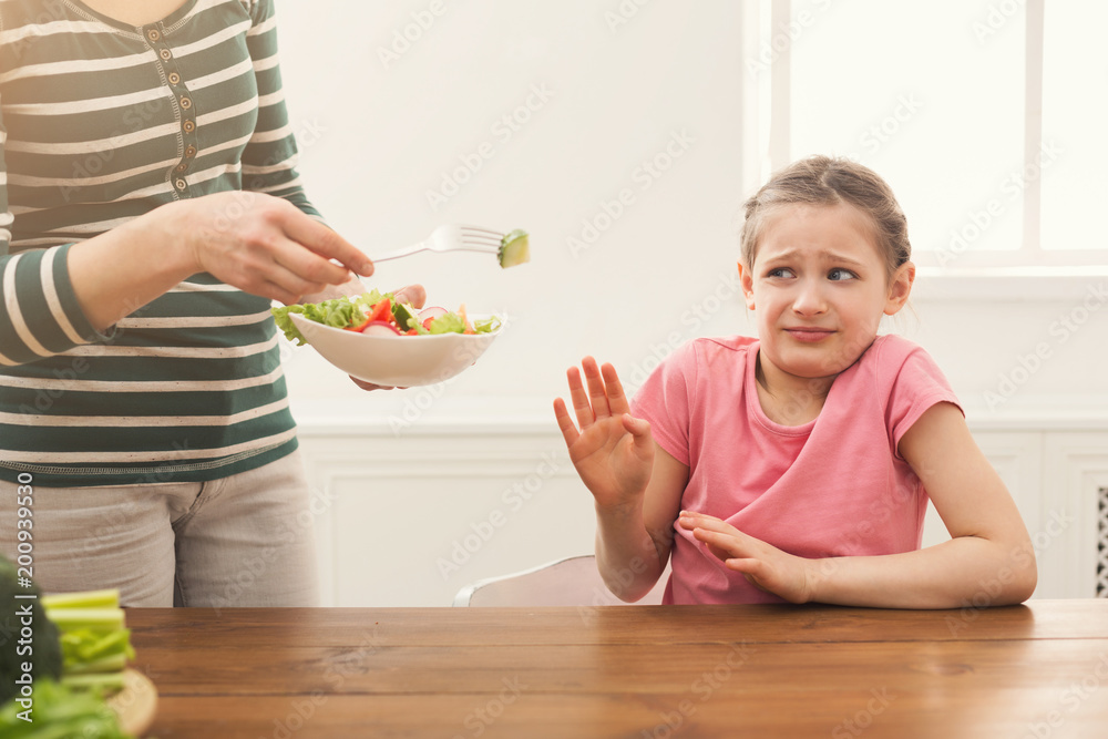 Woman offering her daughter salad but girl refusing Woman offering her daughter salad but girl refusing