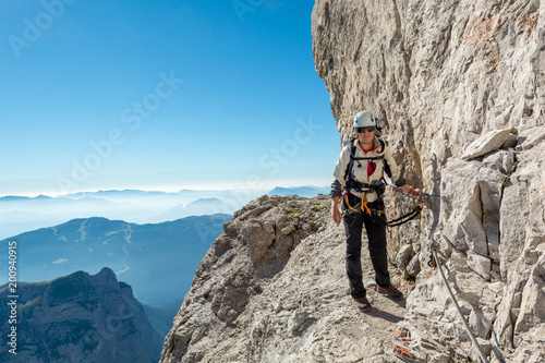 Vászonkép Happy female mountaineer climbing via ferrata.