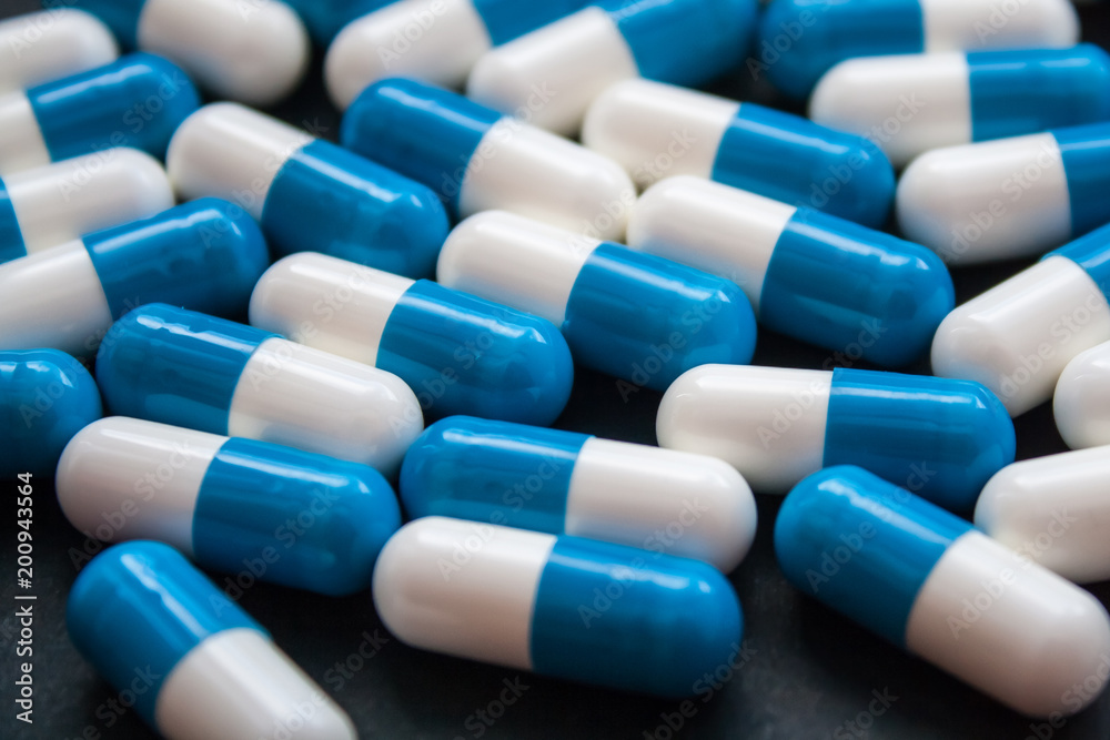 Blue and white pills or capsules on black background close up. Medical concept.