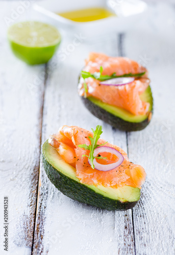Delicious appetizer of avocado and smoked salmon on white wooden background