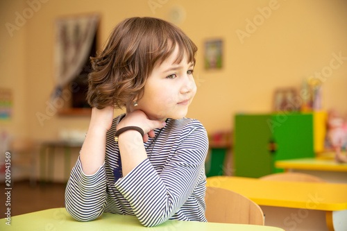 Portrait of cute little girl sitting with hands clasped at desk in classroom