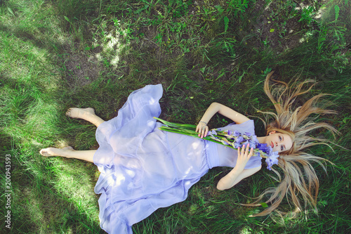 Attractive young girl with blonde dren hair and natural make-up smelling blue purple iris flowers lying on grass outdoors, tenderness and softness on nature background photo