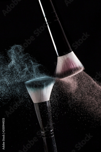 Makeup brushes with red and green powder explode on a black background