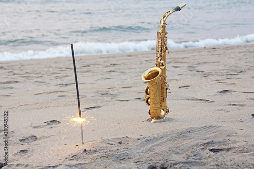 Photography The golden saxophone alto stands on the sand and on the shore, against the background of the sea and Bengal lights