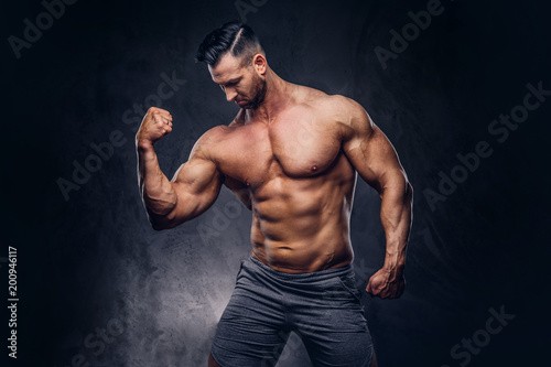 Portrait of a shirtless tall huge male with a muscular body with a stylish haircut and beard, in a sports shorts, posing in a studio. © Fxquadro