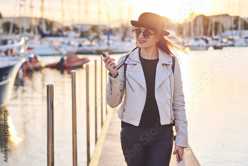 Pretty young woman in black hat with vape at a sea port photo