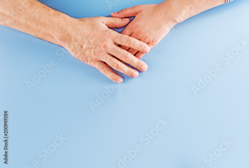 The hand of an adult father covers the child's hand. Attachment concept on a sky blue background with copy space