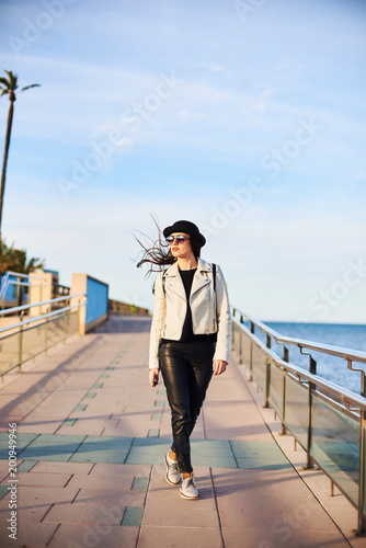 Pretty young woman in black hat walking by the sea