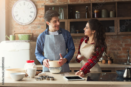 Happy young woman and man baking in loft kitchen