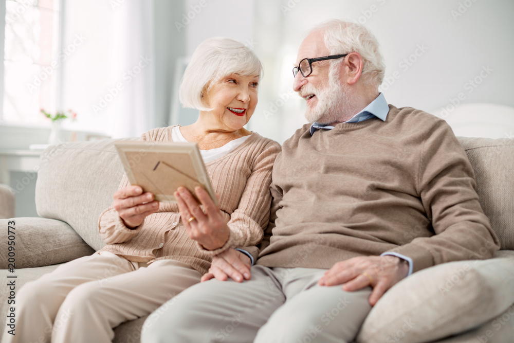 Our memories. Nice pleasant elderly woman holding a photograph while sitting together with her husband Our memories. Nice pleasant elderly woman holding a photograph while sitting together with her husband