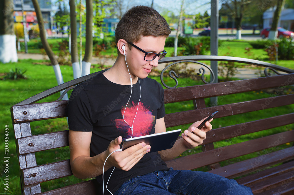 Obraz premium A young guy in the Park uses gadgets, smartphone and tablet