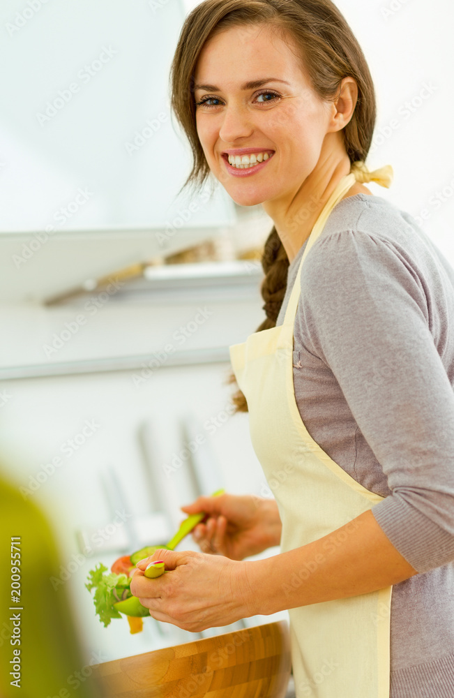 Smiling young housewife mixing salad in modern kitchen