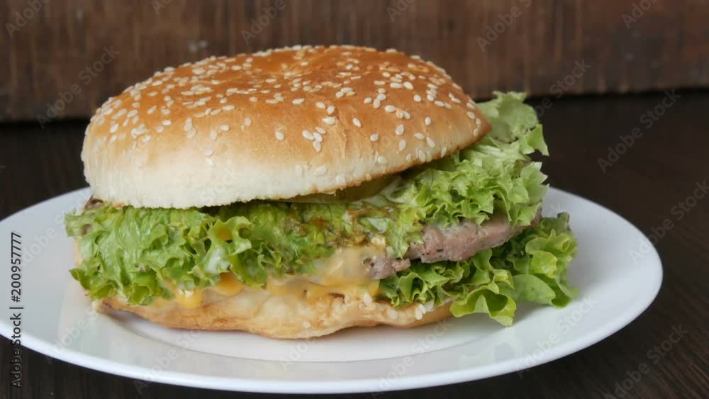 Large triple burger with lettuce leaves on a white plate. Hamburger on a stylish wooden background. Fast food Large triple burger with lettuce leaves on a white plate. Hamburger on a stylish wooden background. Fast food