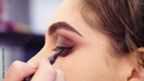 Extreme close up portrait of the woman in the beauty salon. Professional makeup artist painting black eyeliner on the eyes of the model